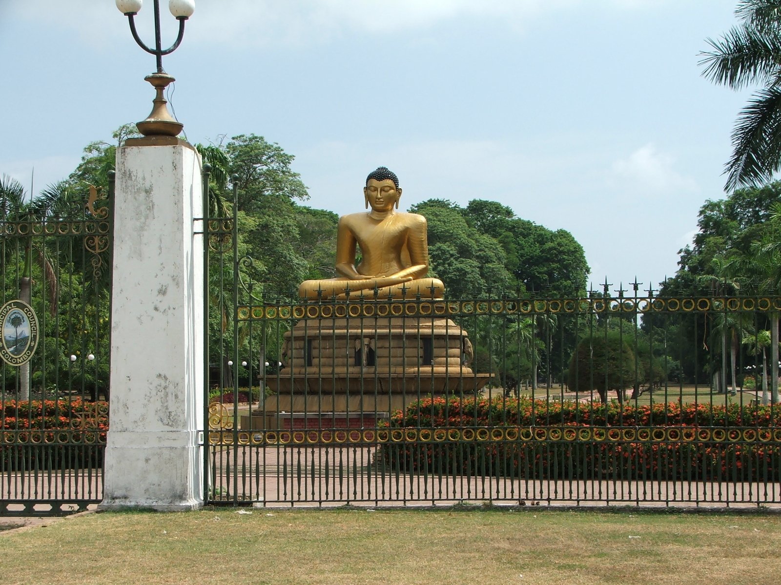 a statue of buddha is behind the fence in front of some bushes