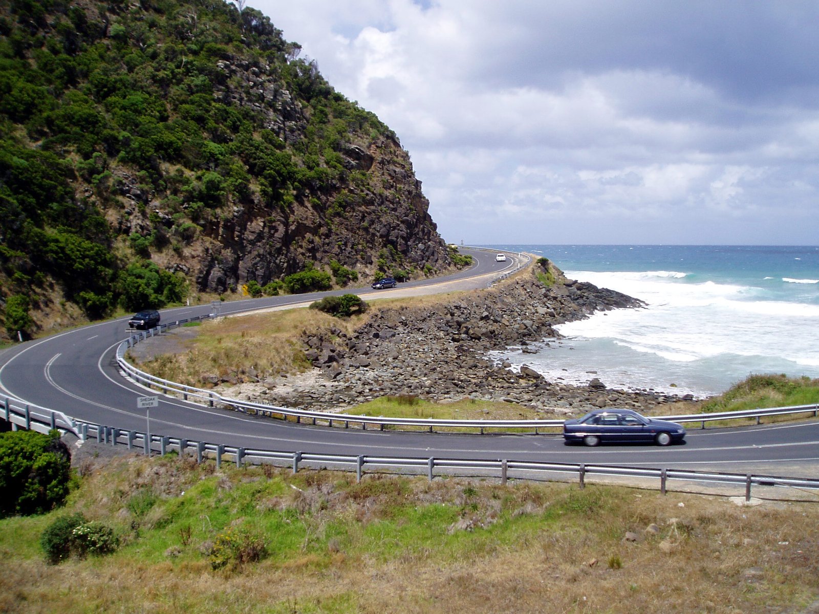 a car driving down a coastal road next to the ocean