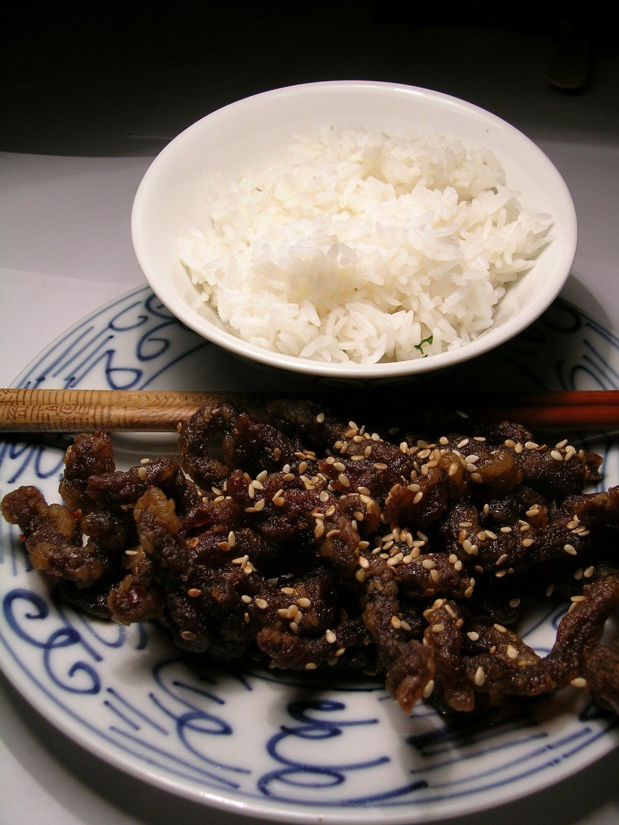 a plate filled with meat and rice next to chop sticks