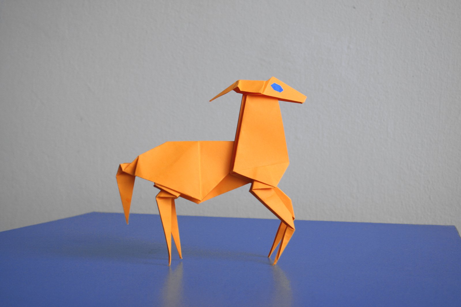 an origami giraffe standing upright on a blue surface