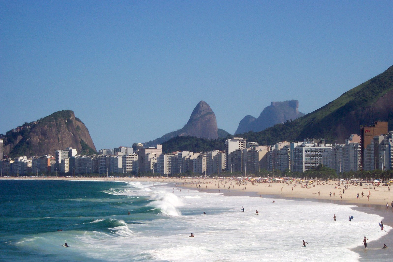 a sandy beach in a city with many swimmers