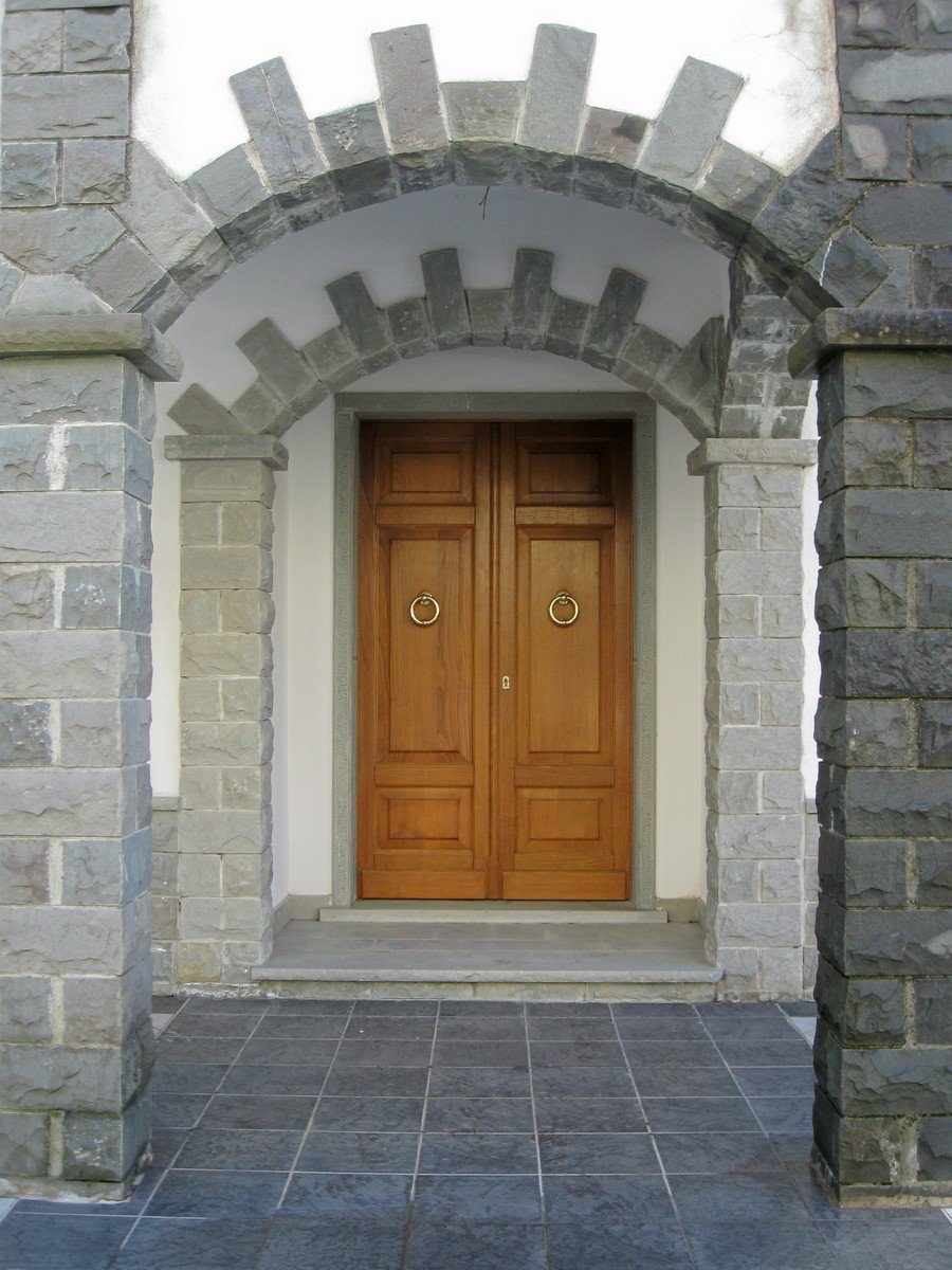 a double wooden door is seen between two stone archways