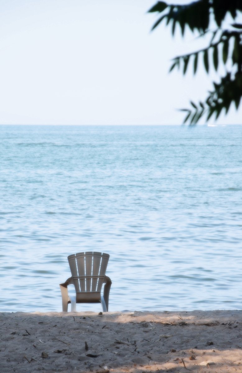 a chair sitting on the beach looking out at a body of water