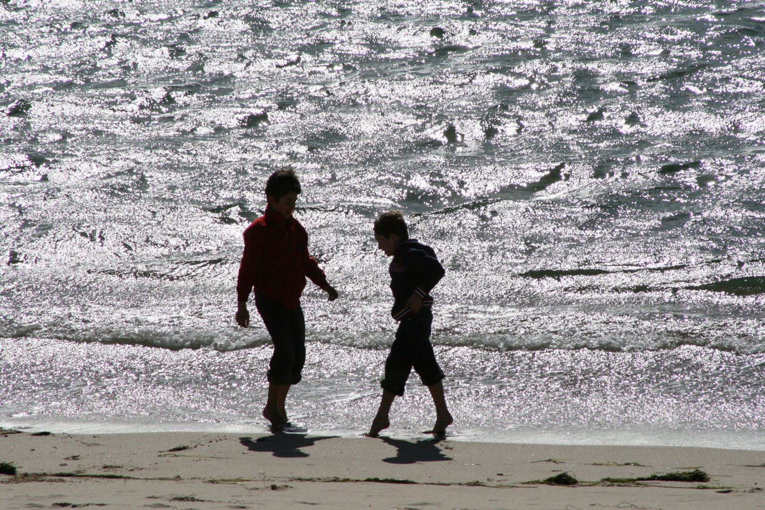 two people walking on a beach near the ocean