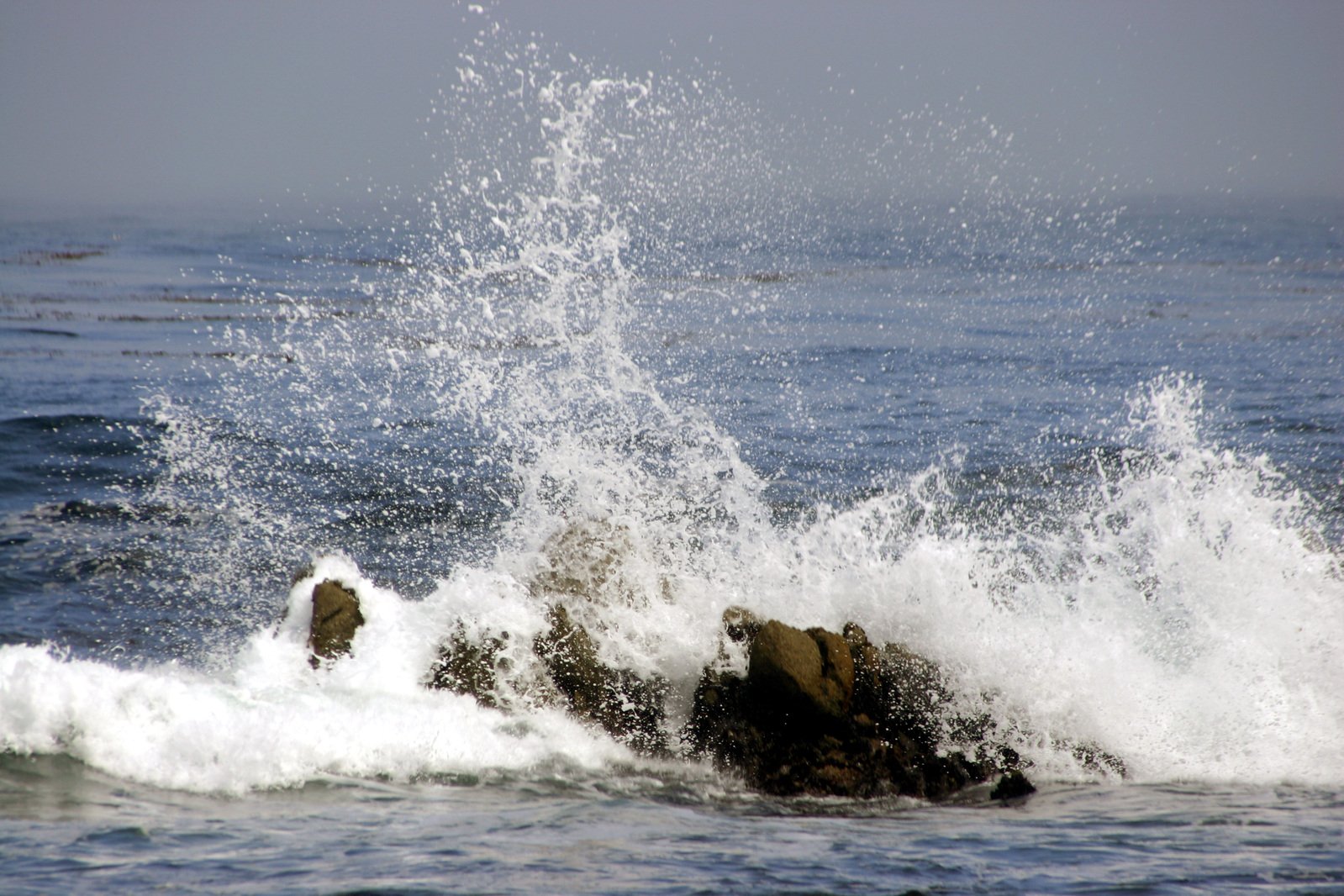 some water splashes onto the shore, near a rock in the ocean