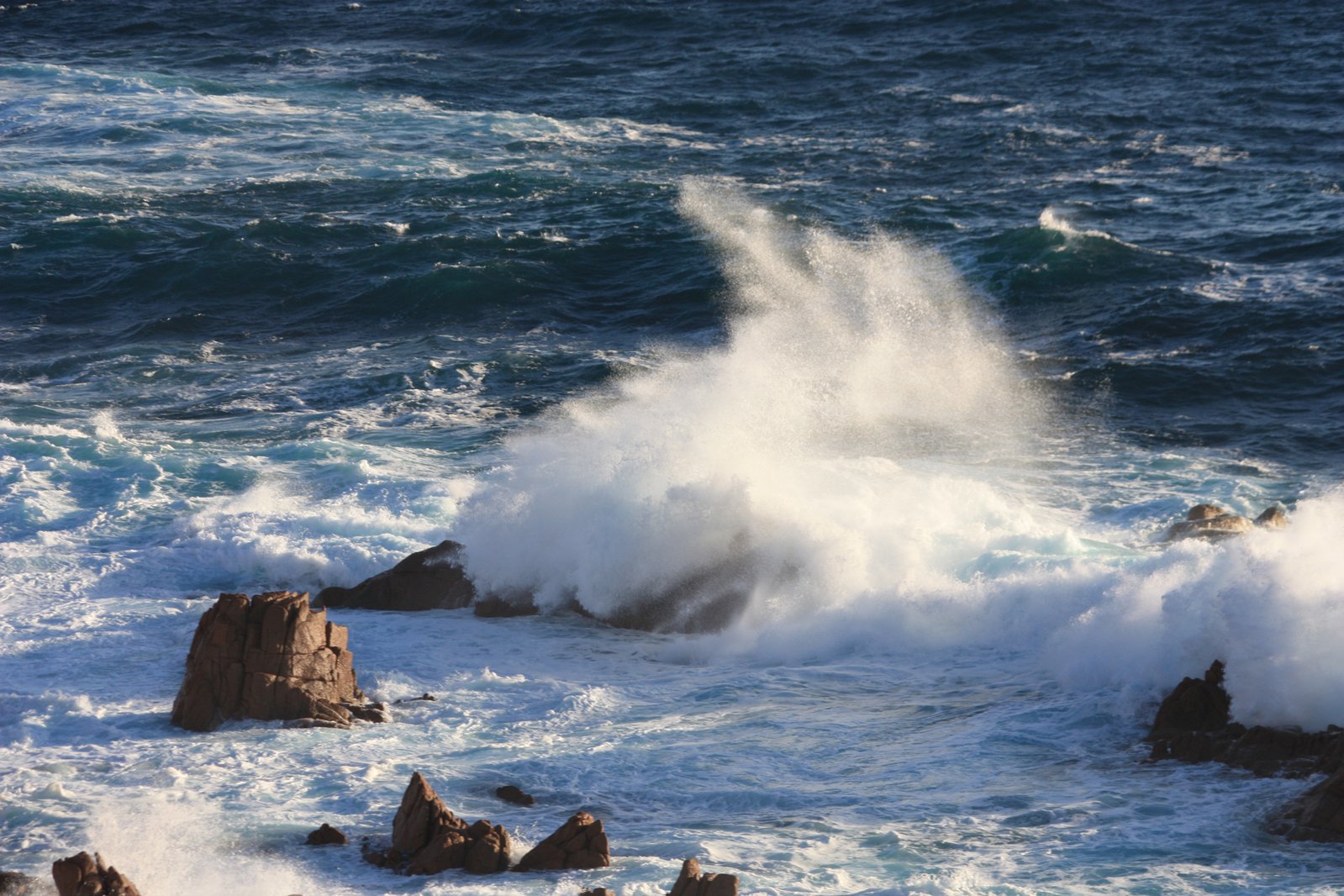 a big ocean wave hitting rocks and crashing into the water