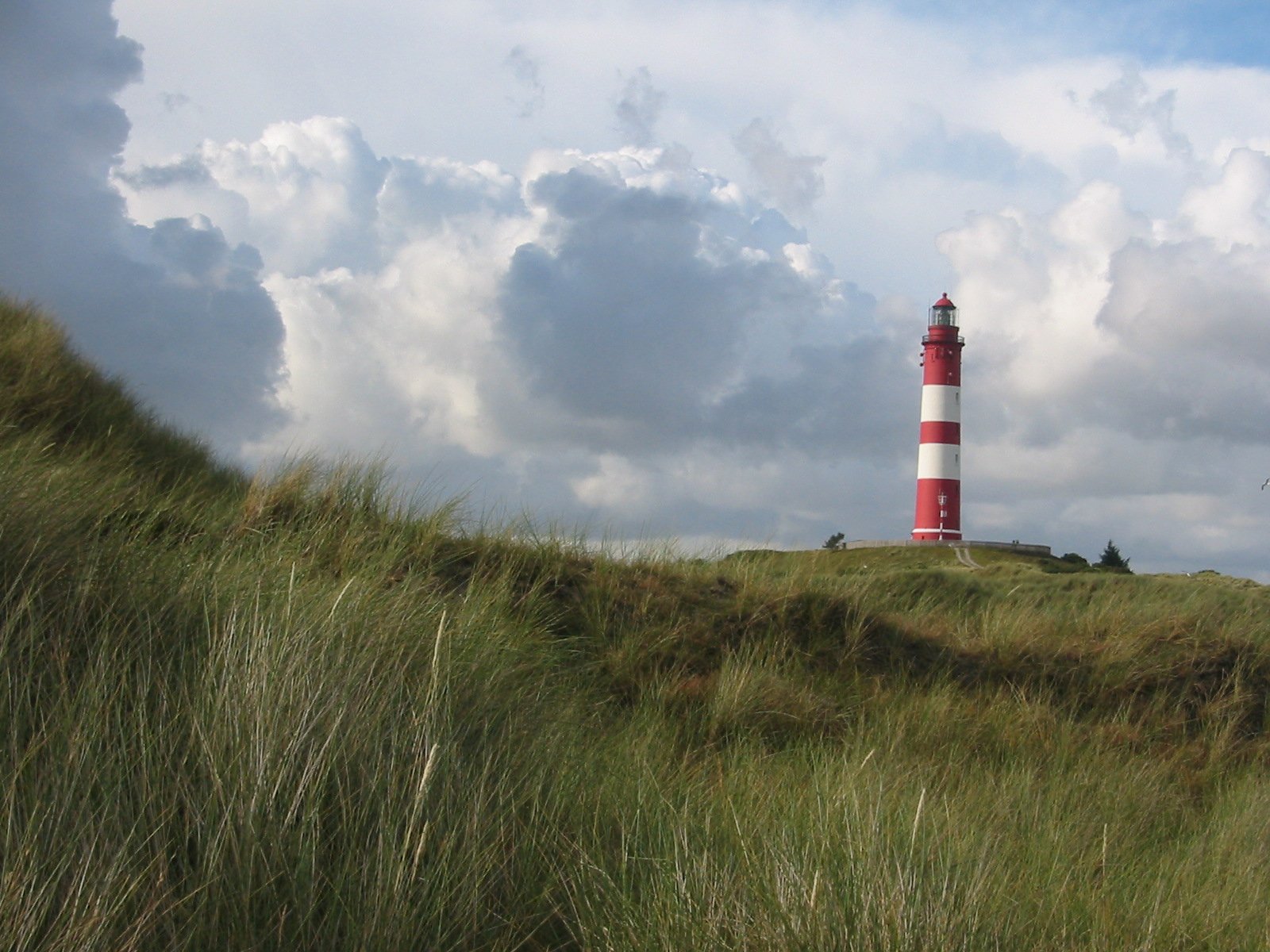 the lighthouse is next to the hill with a sky in the background