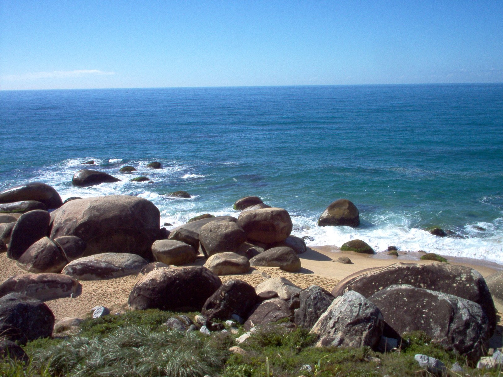 the beach has large boulders and ocean in the background