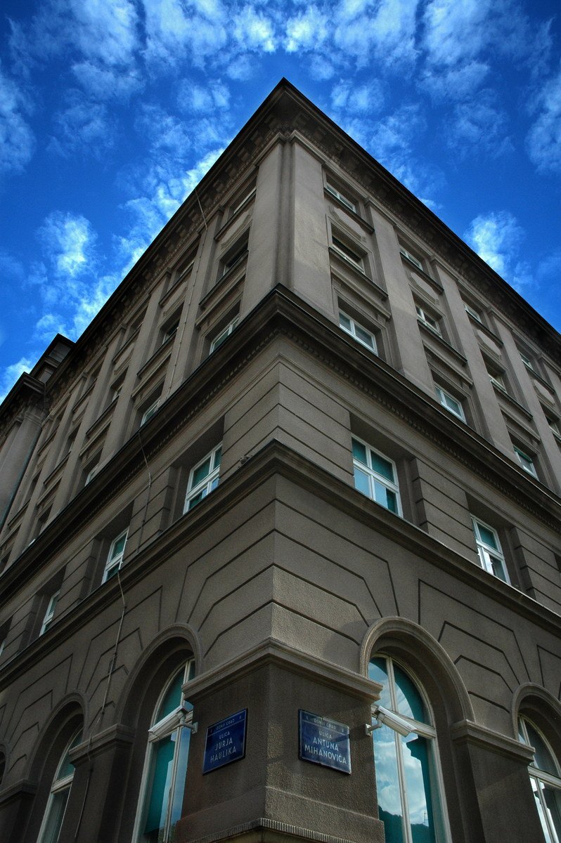 a tall, beige building stands beneath a blue sky with wispy clouds