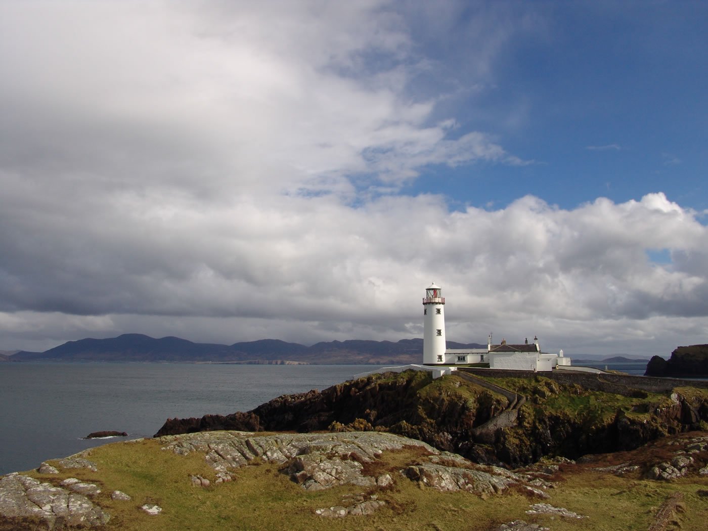 the lighthouse is on top of the cliff and a dark cloudy sky hangs over the water