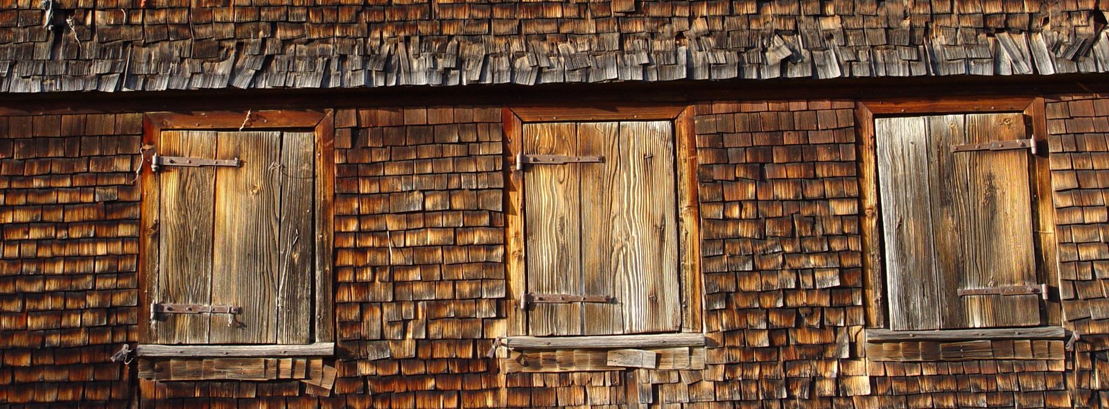 three wood windows sit on the side of an old wooden building
