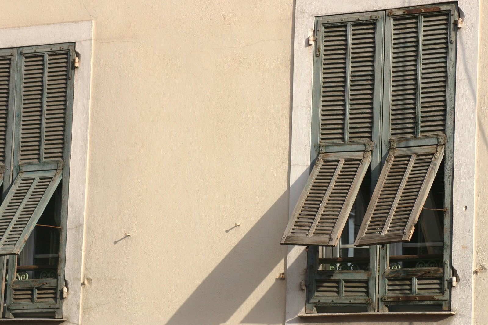 the two windows with closed wooden shutters are next to each other