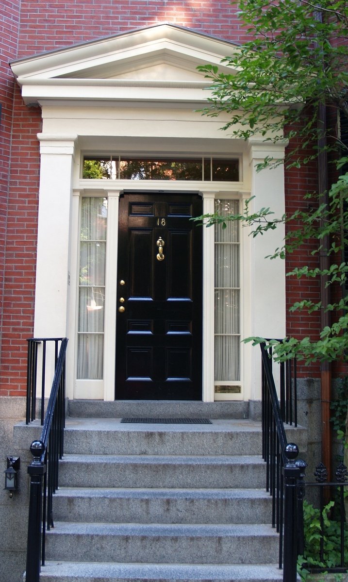 a set of steps with a black door, with a white window and some plants