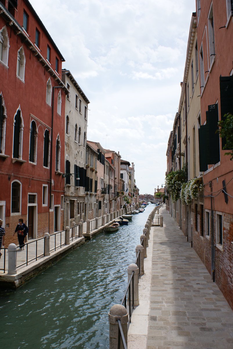 a narrow waterway in between buildings with one person on bike and another boat