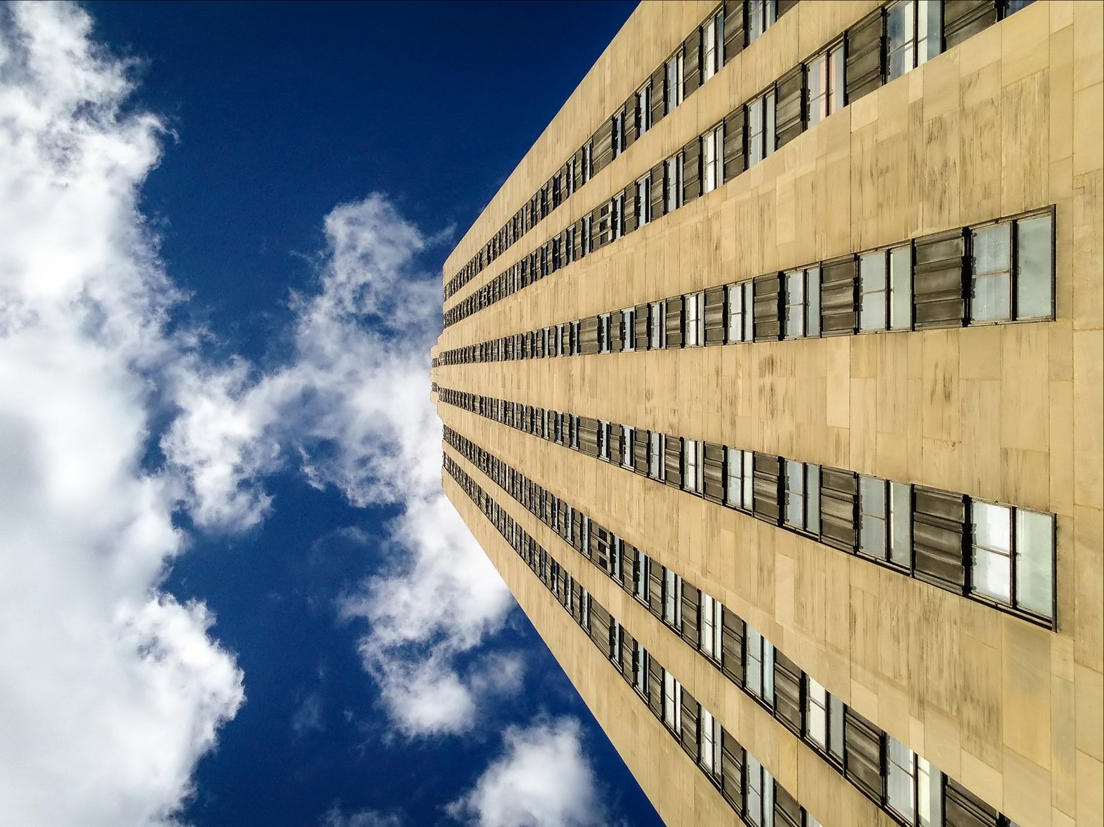 a tall building with windows on the front, and clouds in the background