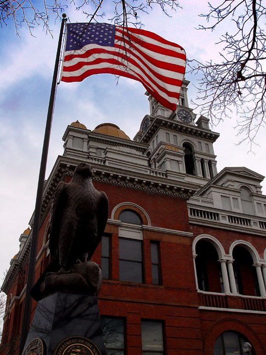 a large eagle statue stands with an american flag flying in the background