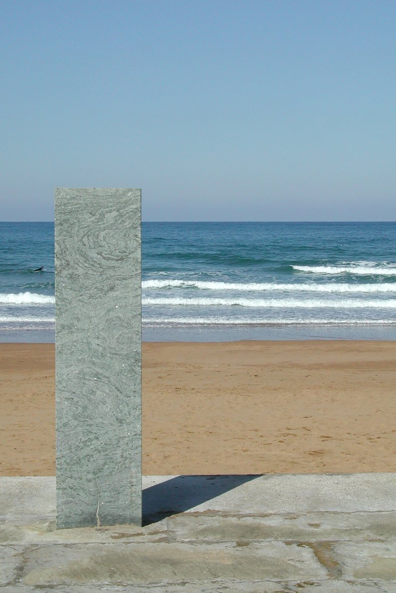 a cement monument with a white vase sitting next to it in the sand near a beach