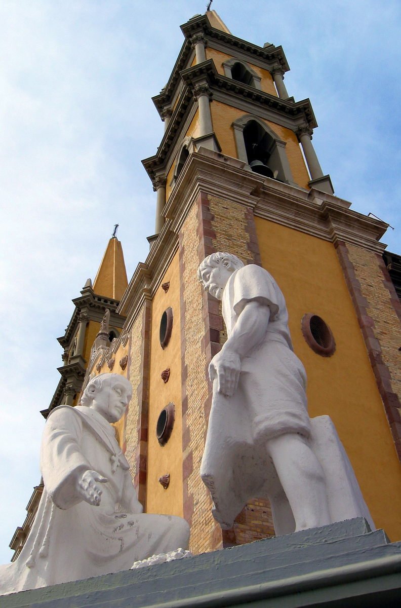 a tall brown clock tower towering over a white statue