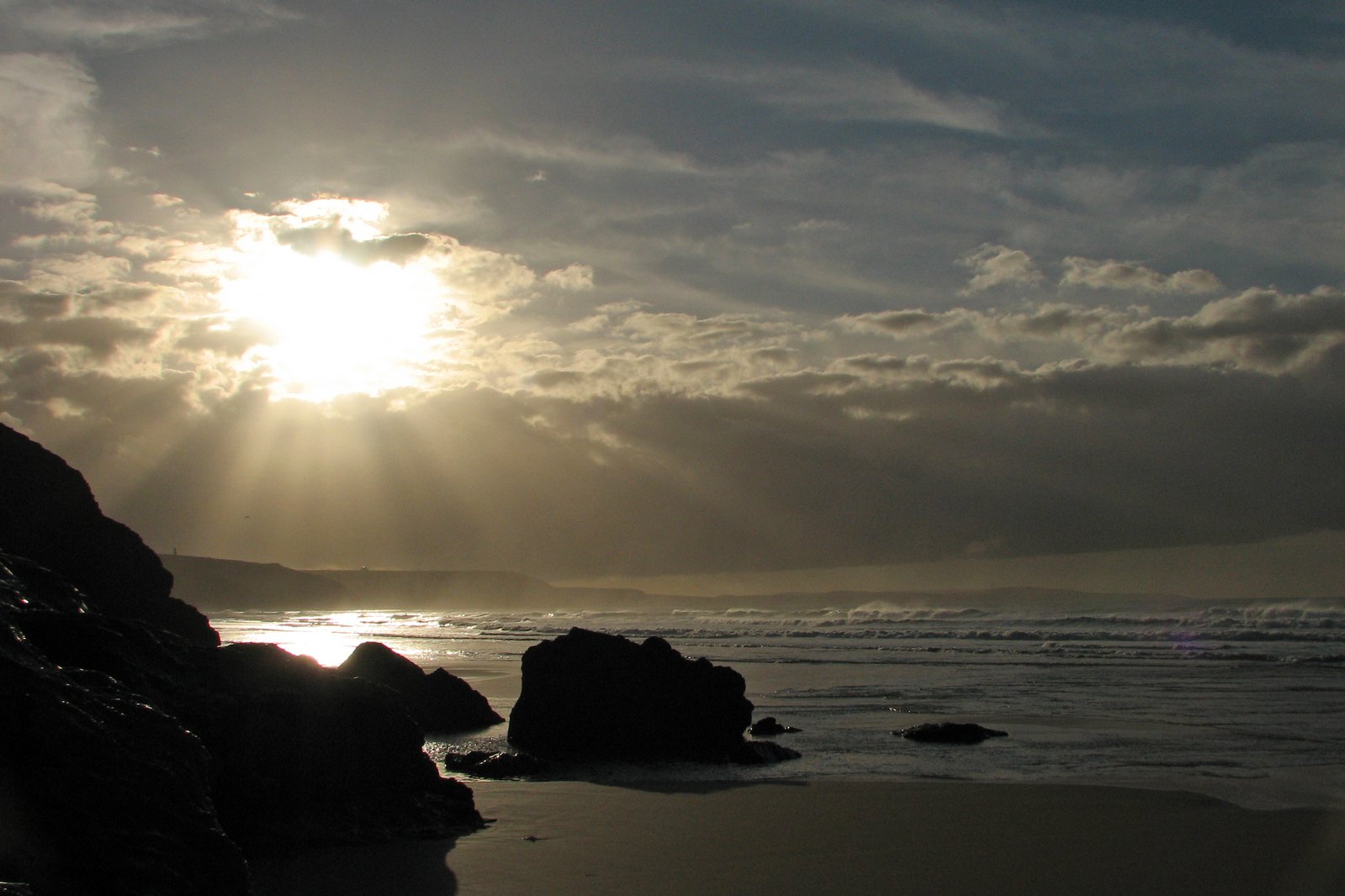 the sun shining through clouds over the ocean on a rocky beach