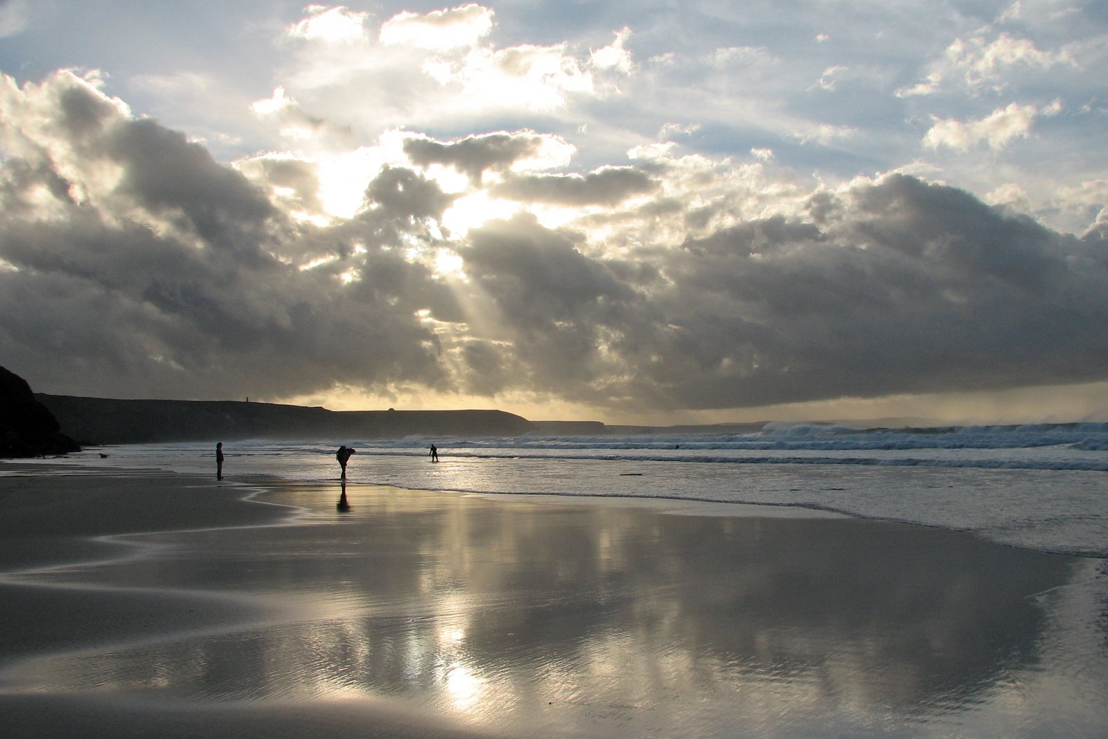 two people walking along the beach under cloudy skies