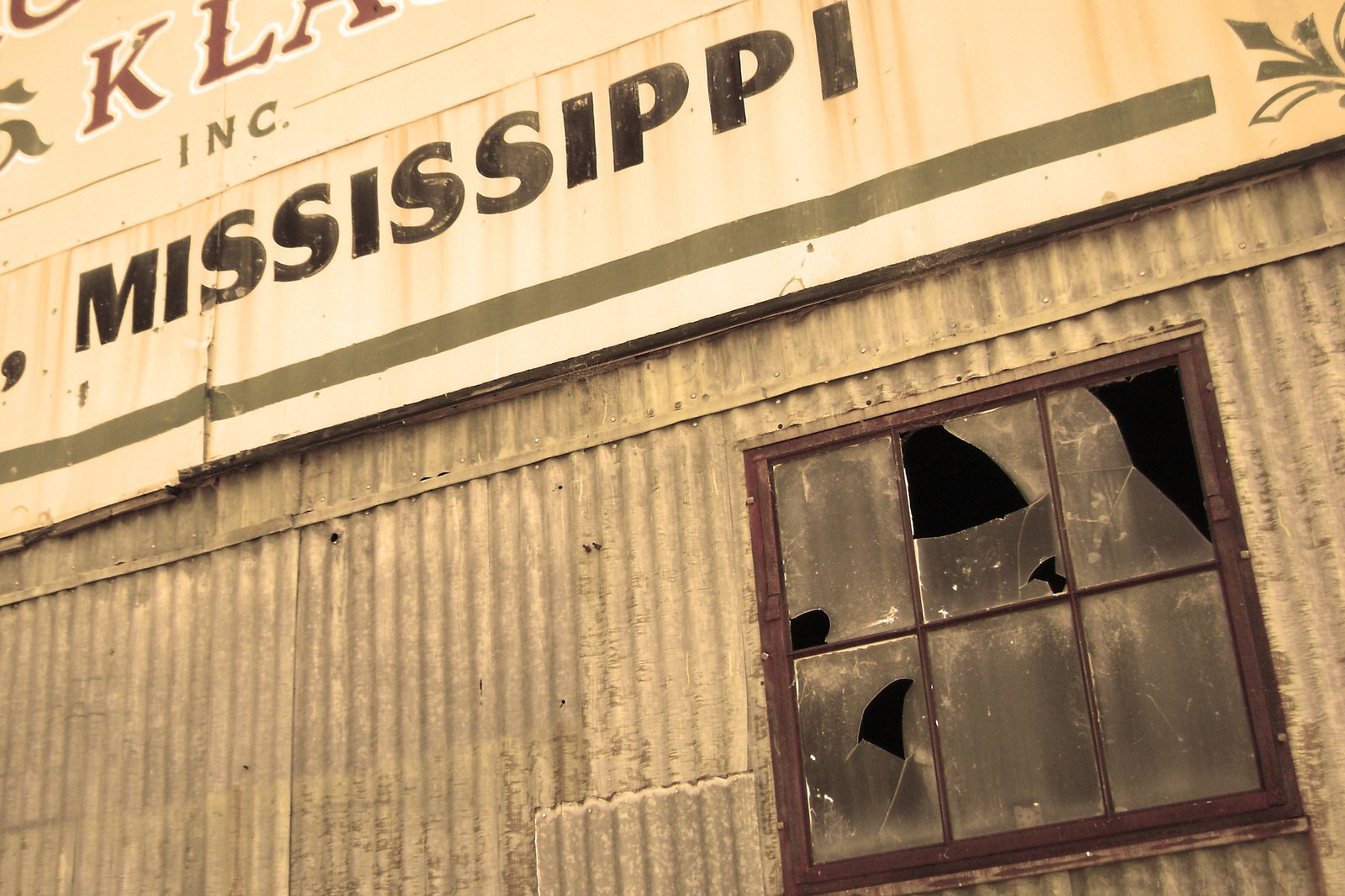 the side of an old rusty building with a broken window