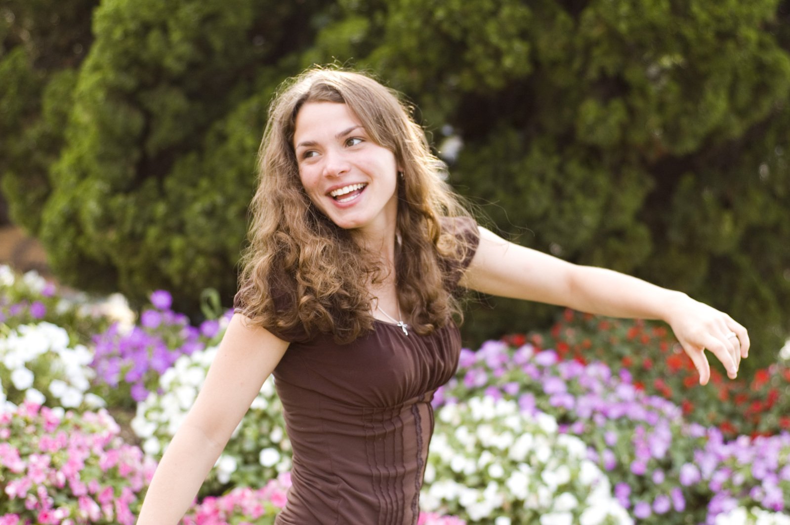 a smiling young woman stands near colorful flowers