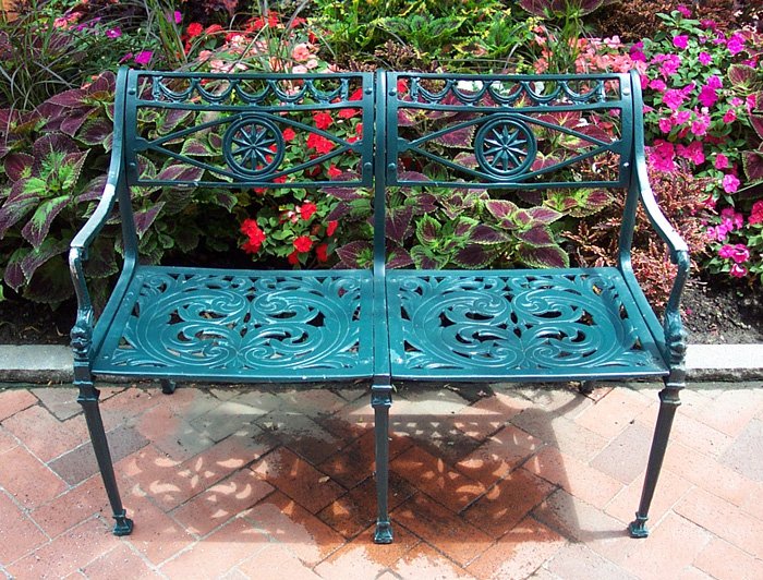 green ornate iron bench in front of colorful flowers