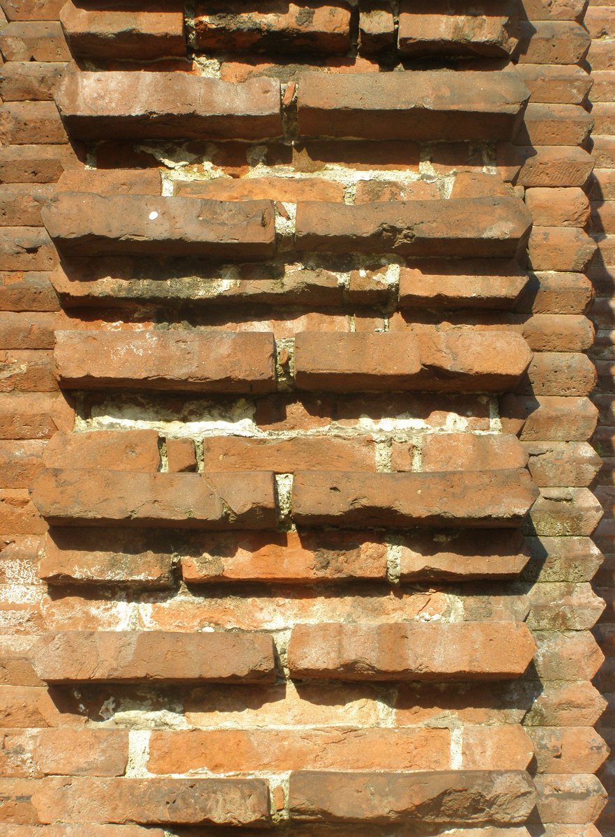 an old brick wall has a green sign at the bottom