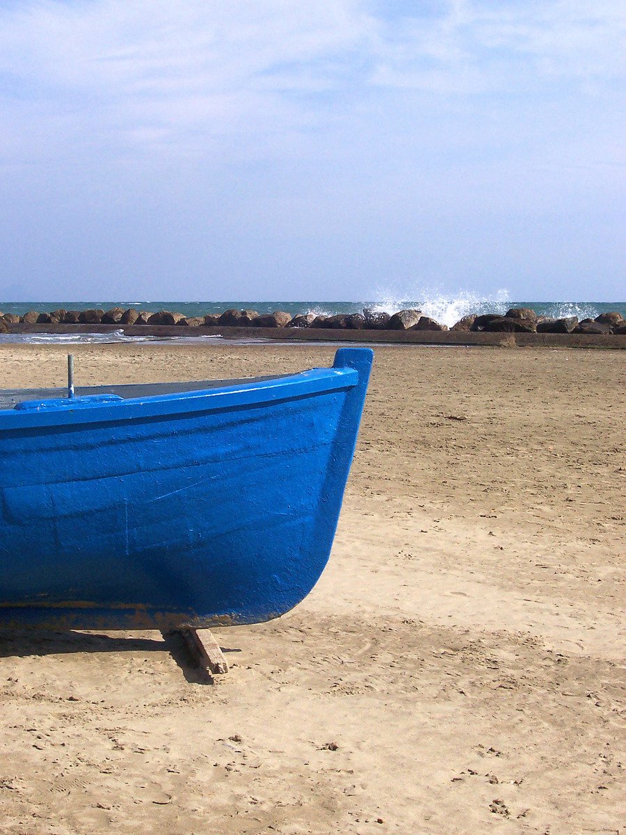 a small blue boat sits on the sand
