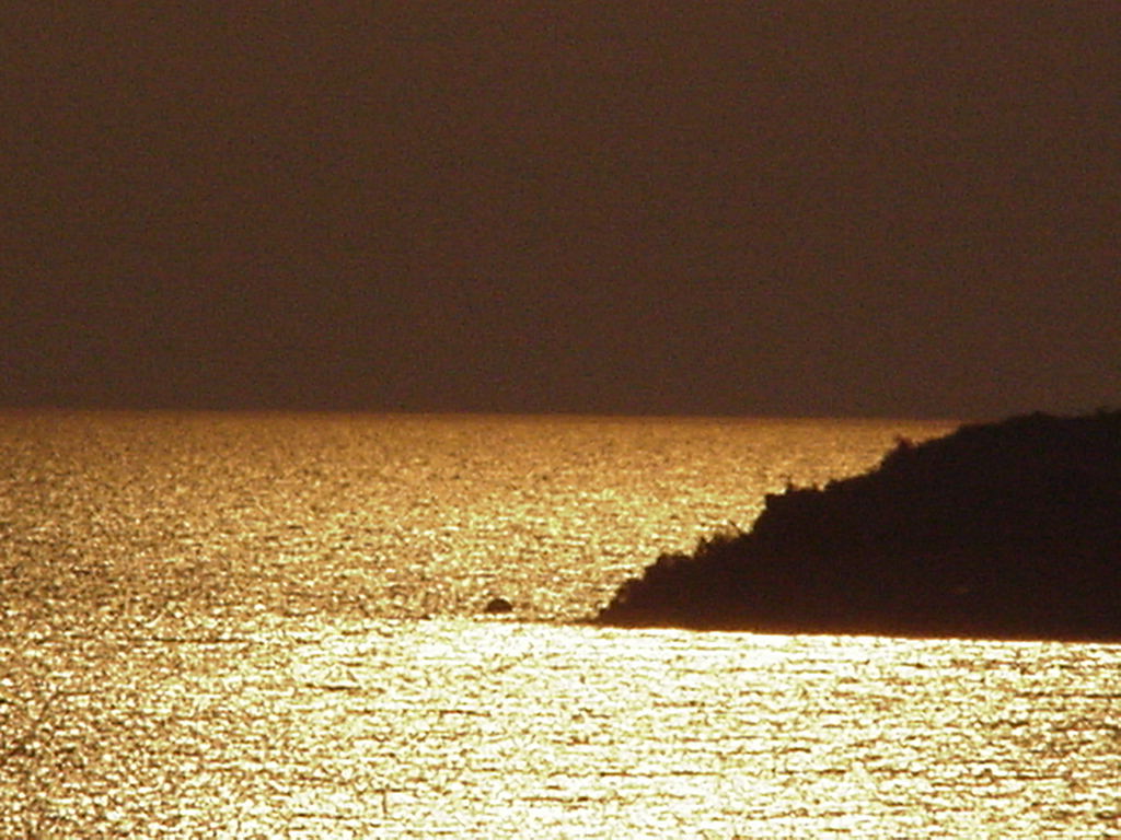 the silhouette of a rock in the water