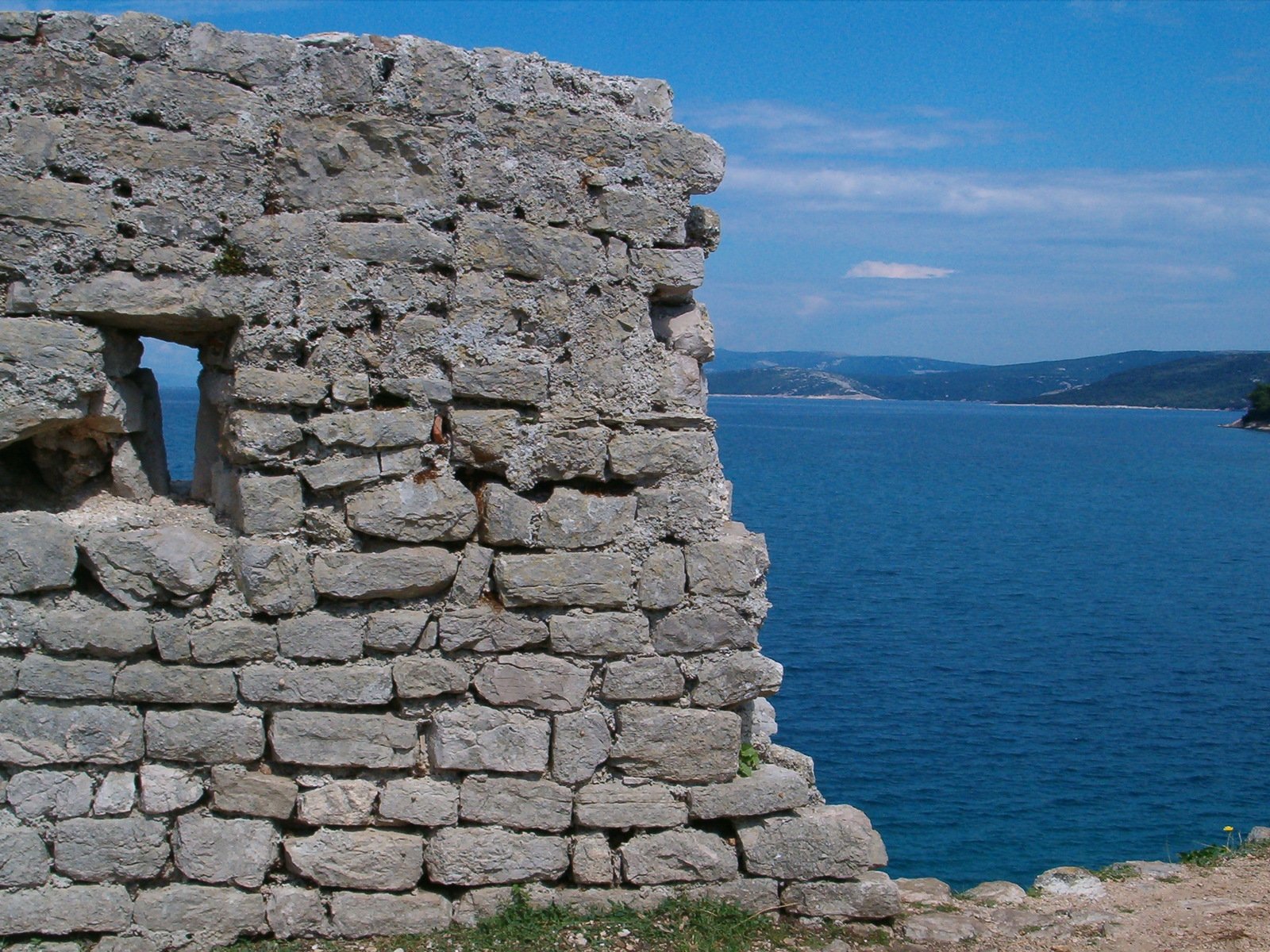 a stone wall by the ocean with a hole in it