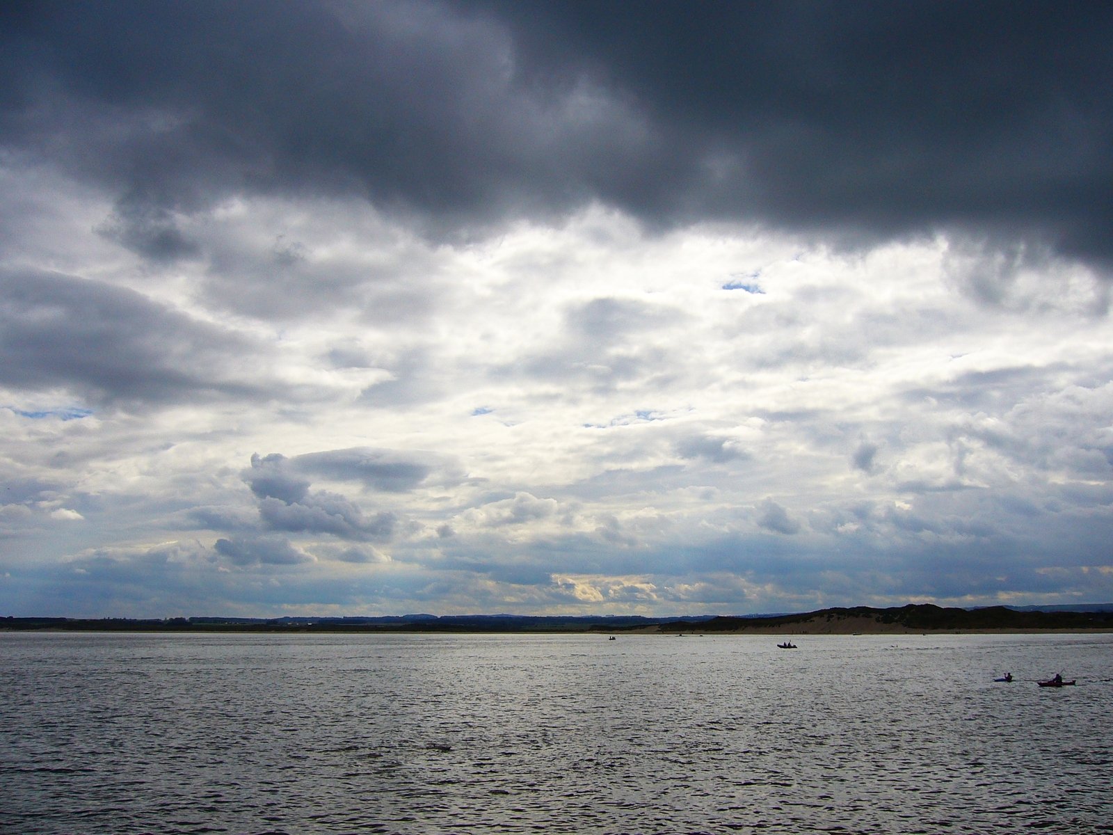 some people riding boats on the ocean under a cloudy sky