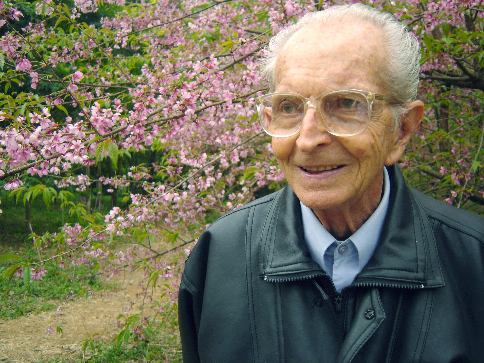 an old man with glasses on standing in front of trees