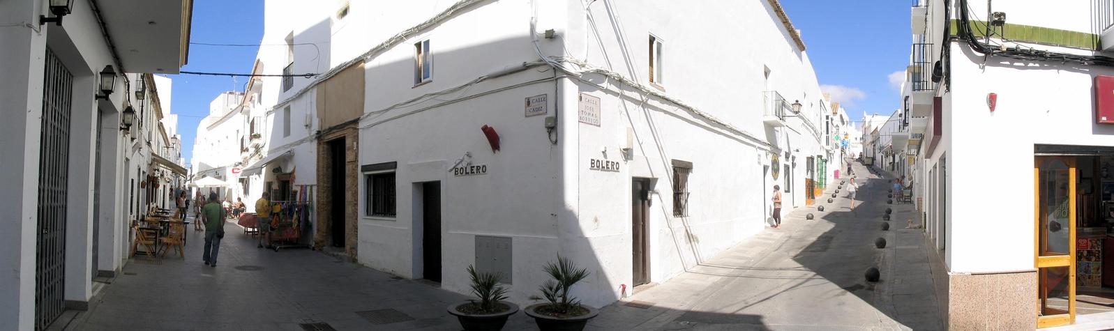 an alley with white building, people walking on either side