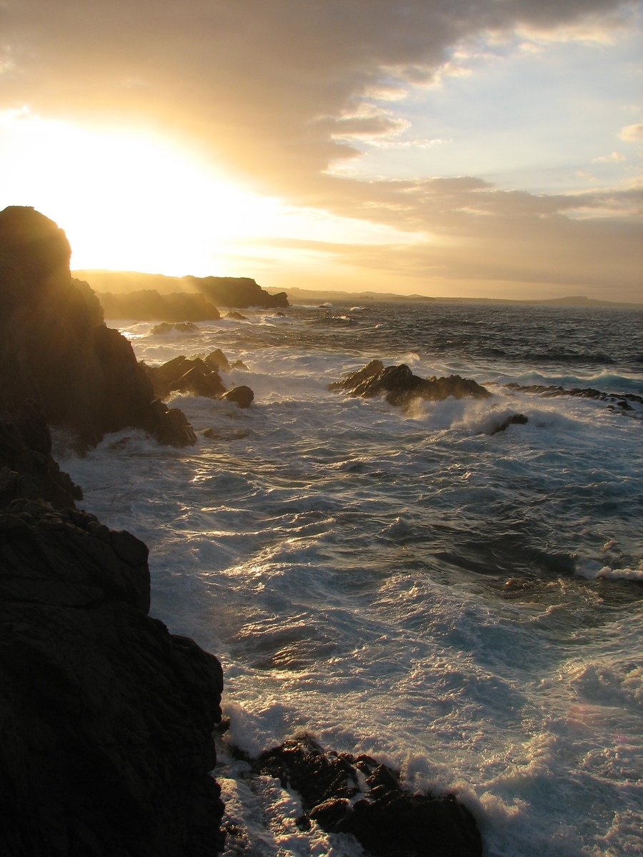 the sun rises over the ocean with a rocky shore