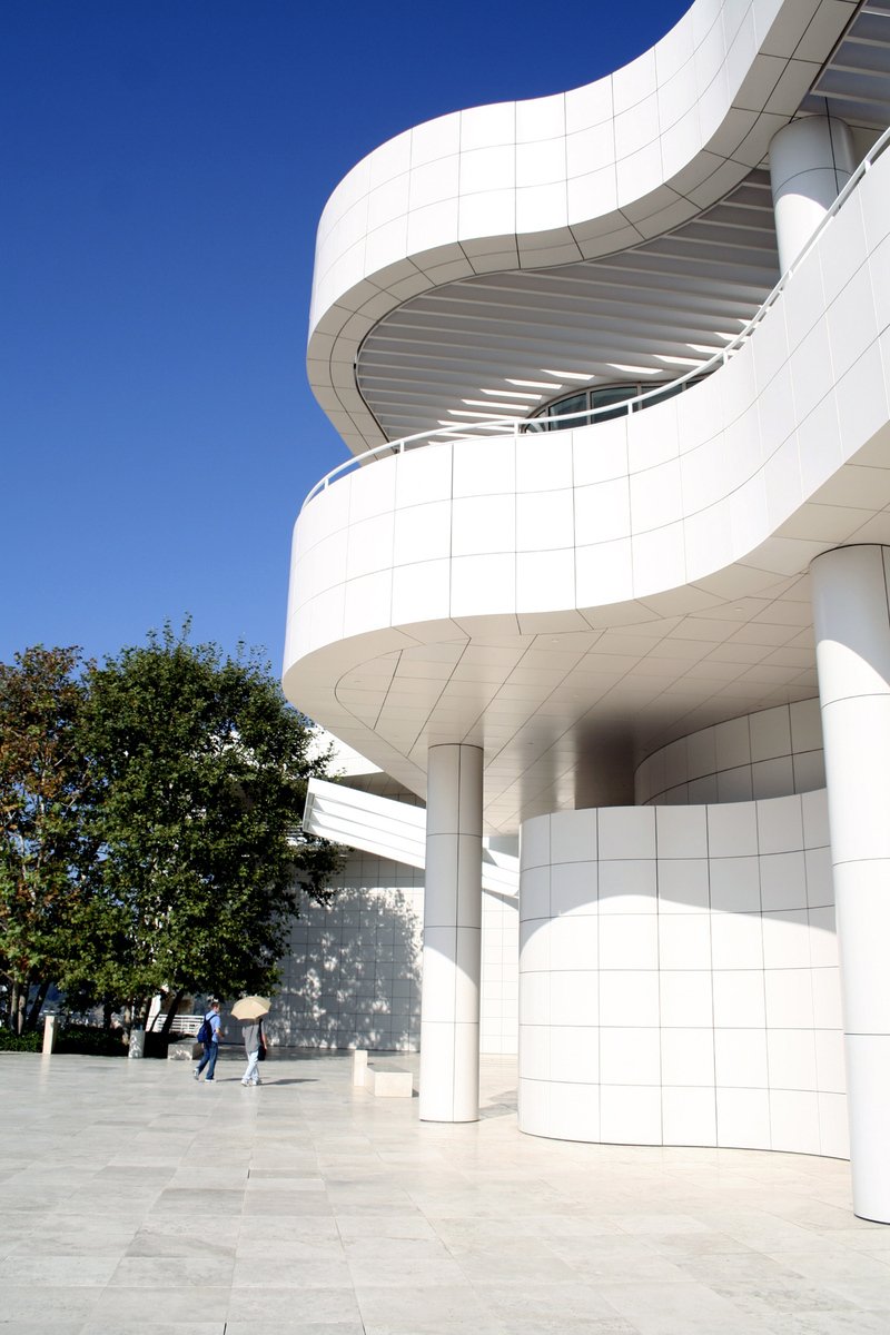 a modern, white curved building sits behind some pedestrians