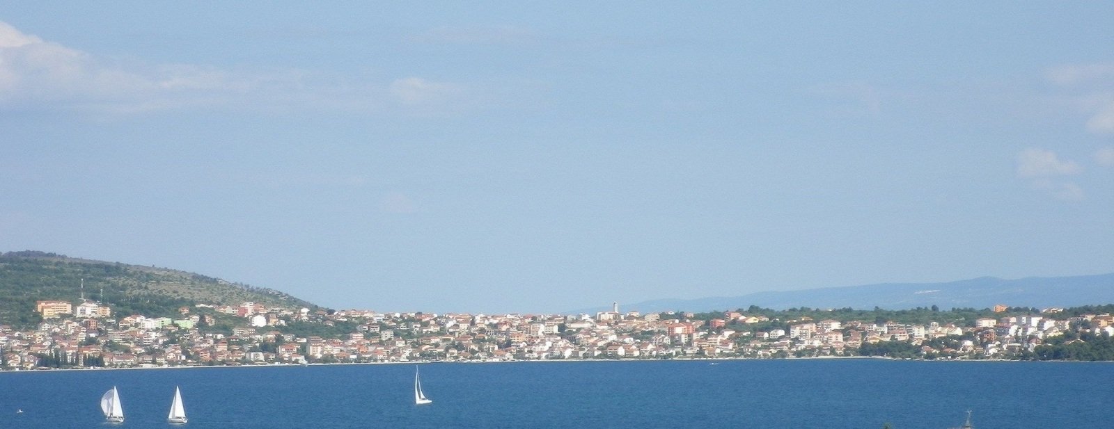 sail boats sailing in the blue ocean and a city on the hillside