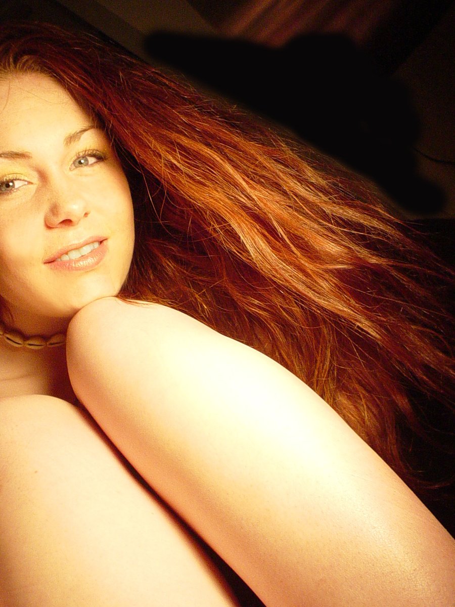 beautiful woman with long red hair sitting on a bed