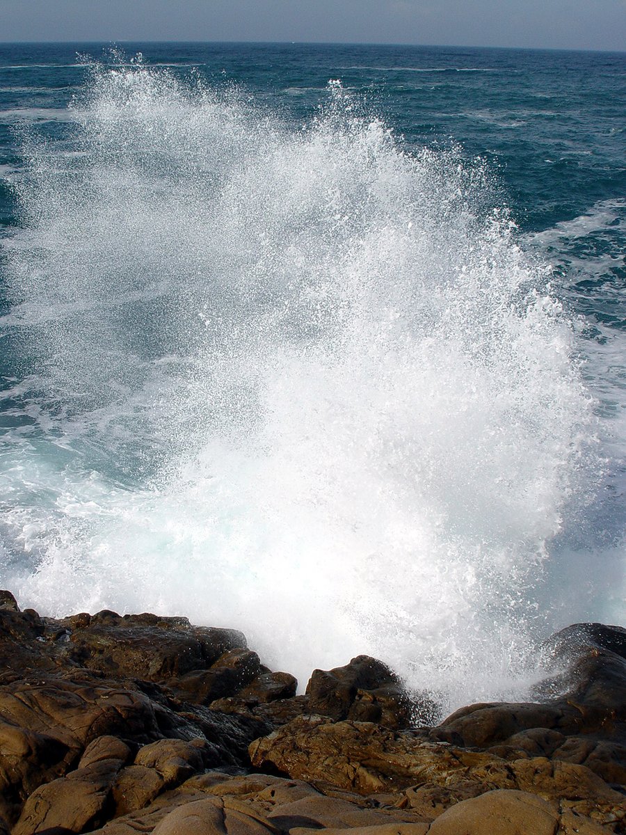 a very large wave hitting onto the rocks by the ocean