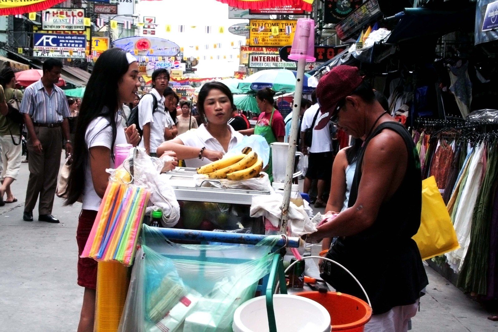 woman working on a fruit stand as two women talk