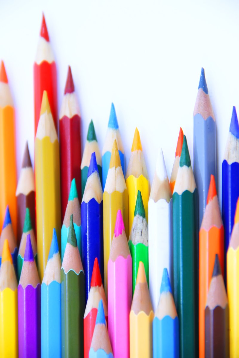 many rainbow colored pencils are in a row and lined against a wall