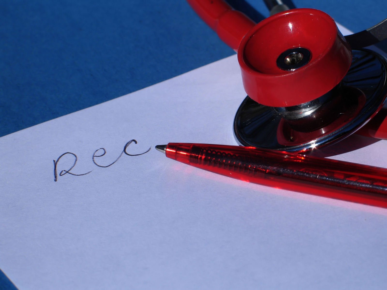 a red stethoscope laying on top of a note reading rec