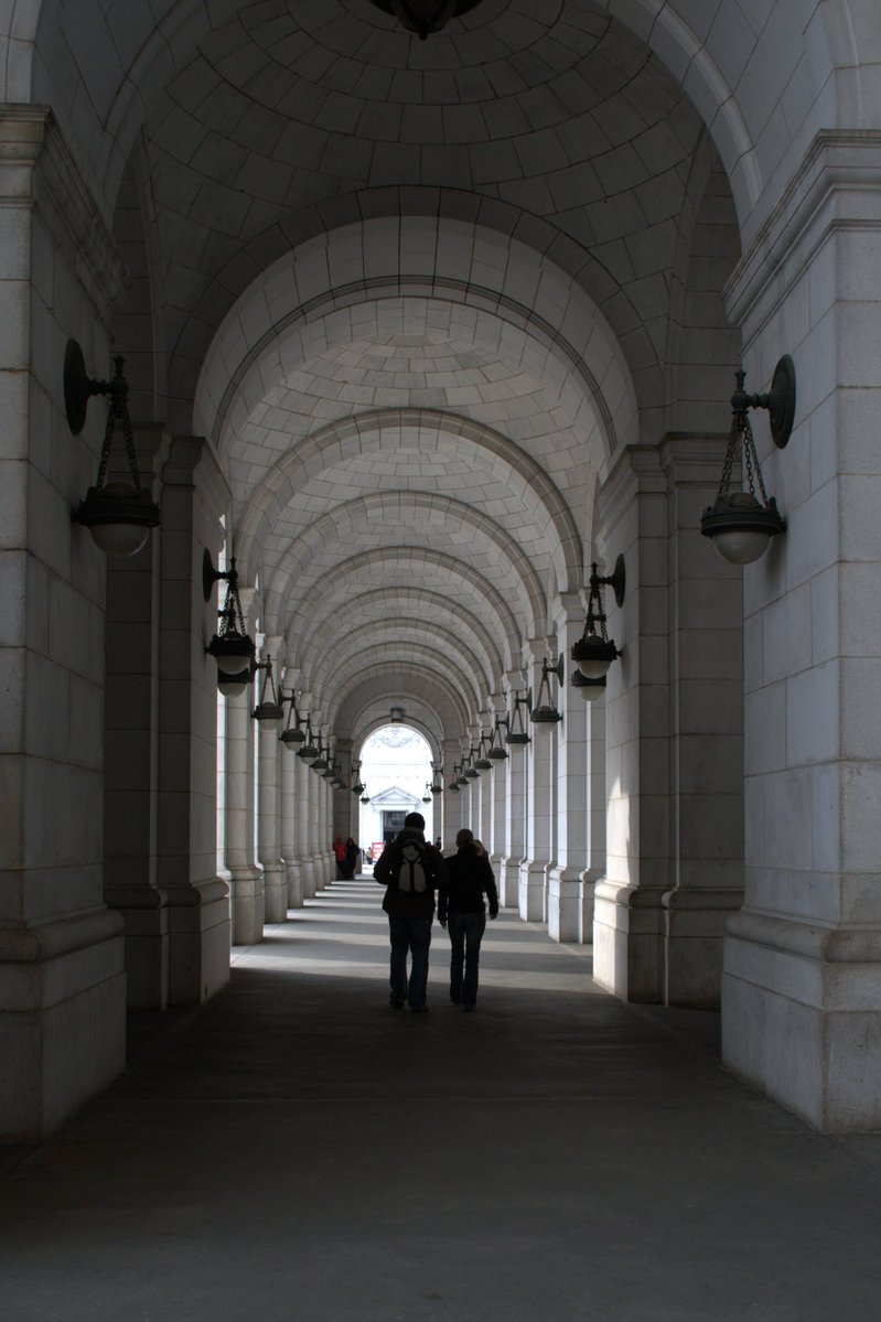 the two people walk down a walkway through an archway