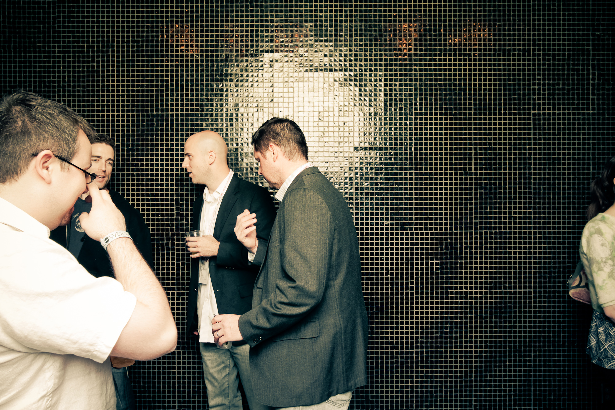 four men stand against a shiny wall in a group