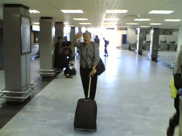 a woman carrying luggage through the airport, smiling