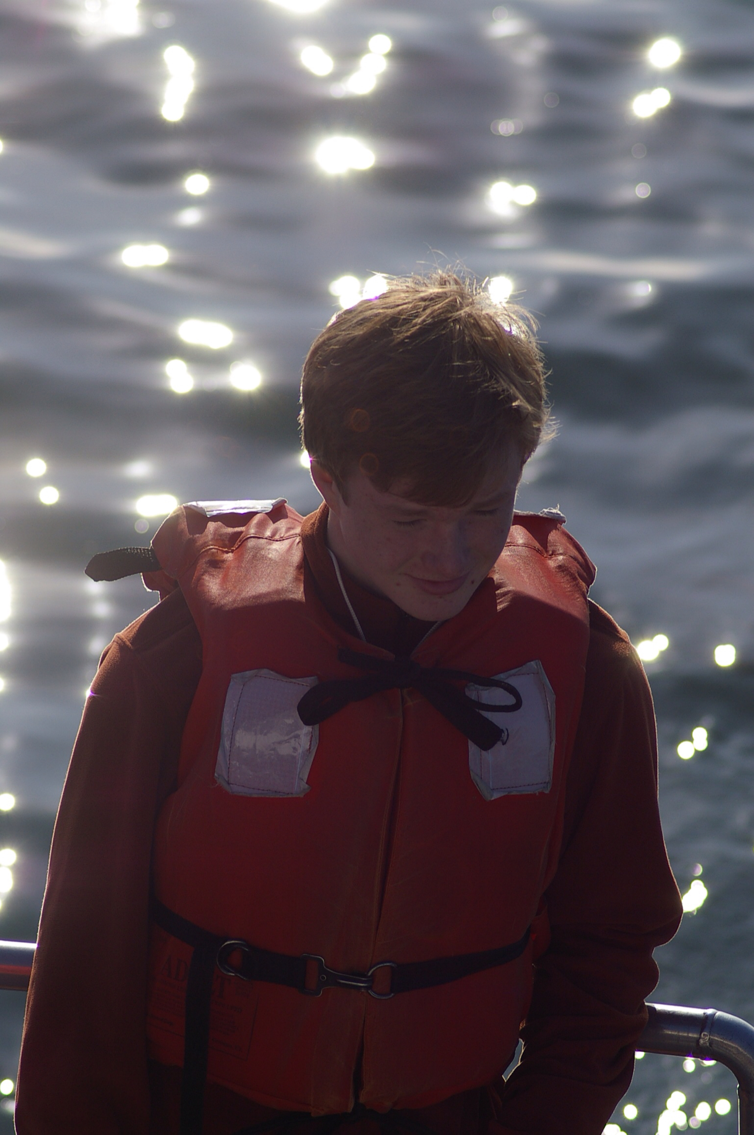 a boy with red life vest on the side of the boat looking at the water