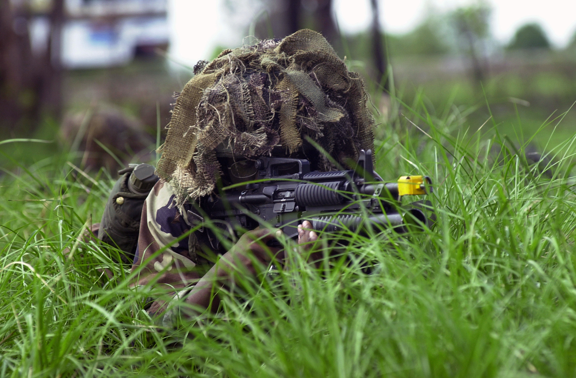 an armed person hiding behind a weapon in the grass