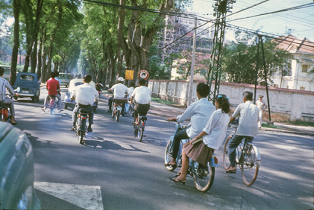 people on bikes riding down a street with trees in the background