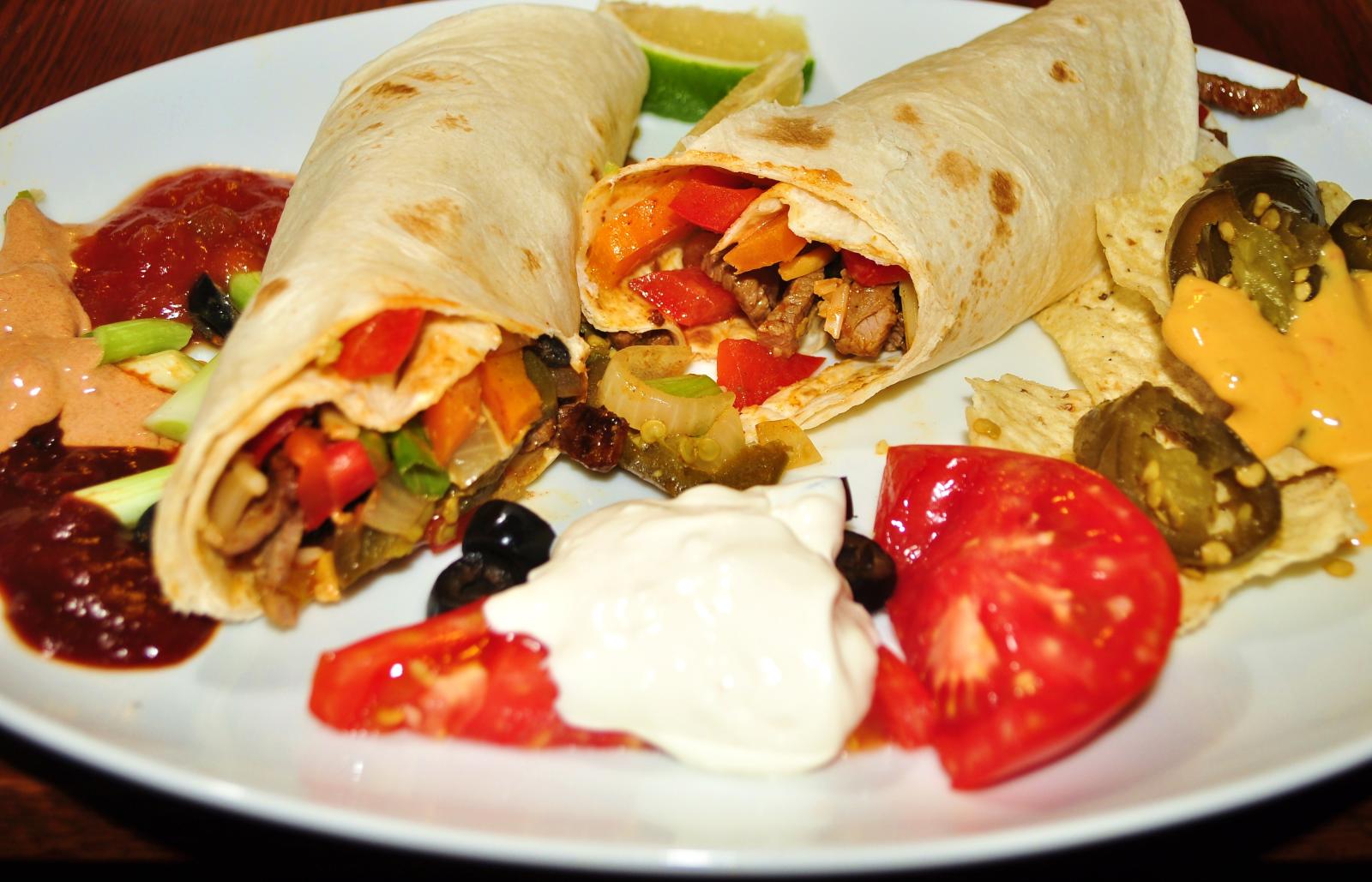 burritos are stuffed with meat, lettuce, tomato, peppers and sour cream