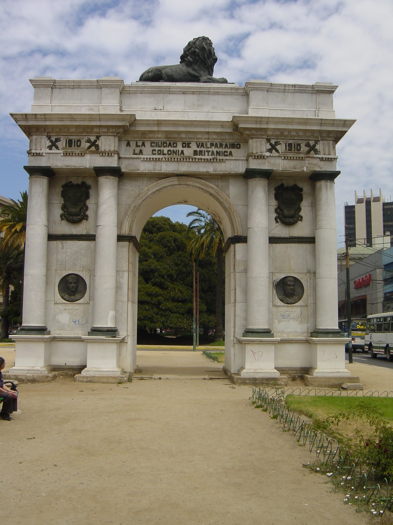 man sitting on bench in front of large arch with lion's head